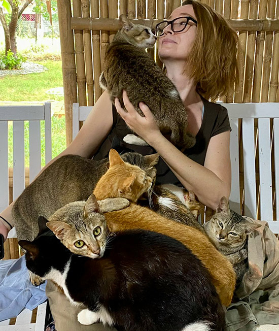 Volunteer cuddling with a group of rescue cats on her lap at Vietnam Cat Welfare shelter